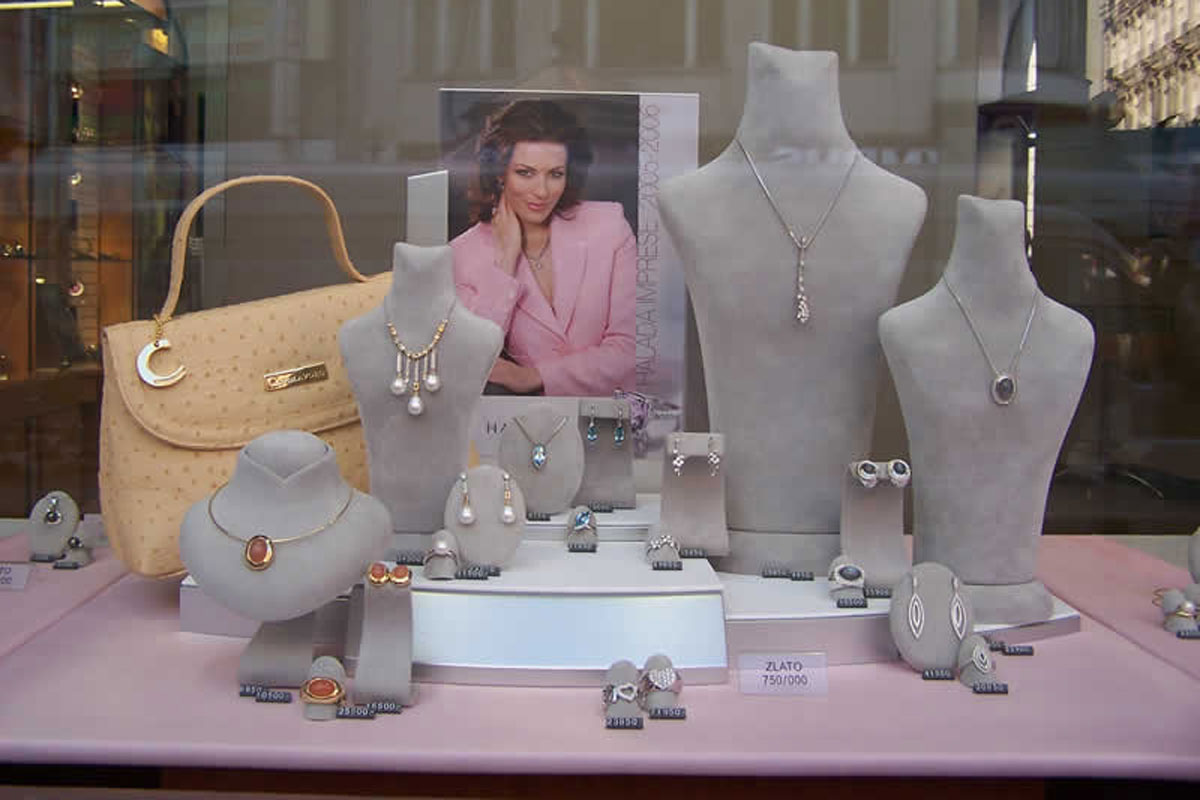 Elegantní šedá torza se šperky, béžová kabelka se zlatou podkovičkou Výloha klenotnictví, kabelka se zlatou podkovičkou pro štěstí, šperky aranžované na elegantním šedém podkladě