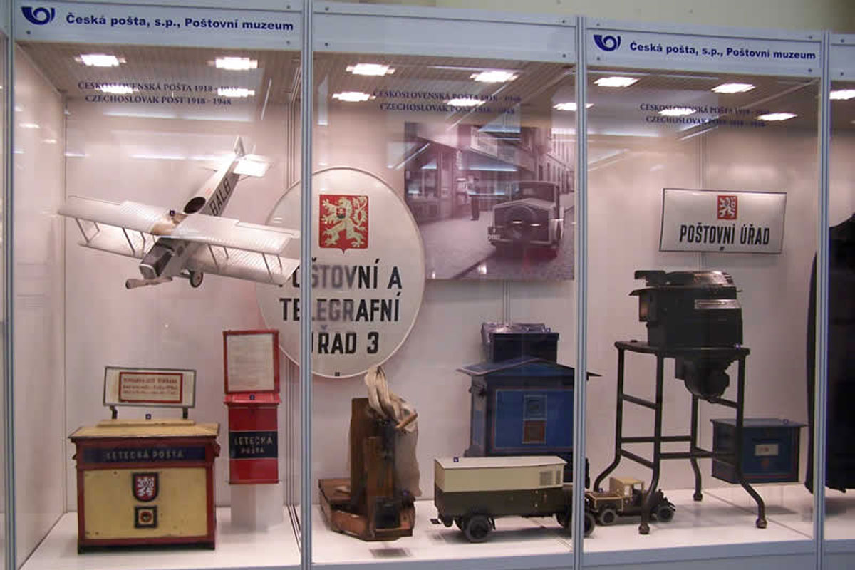 Historické poštovní schránky, makety dopravních prostředků Poštovního úřadu Historické mechanismy pošty, cedule Poštovního úřadu, známky a historické dokumenty ve vitríně