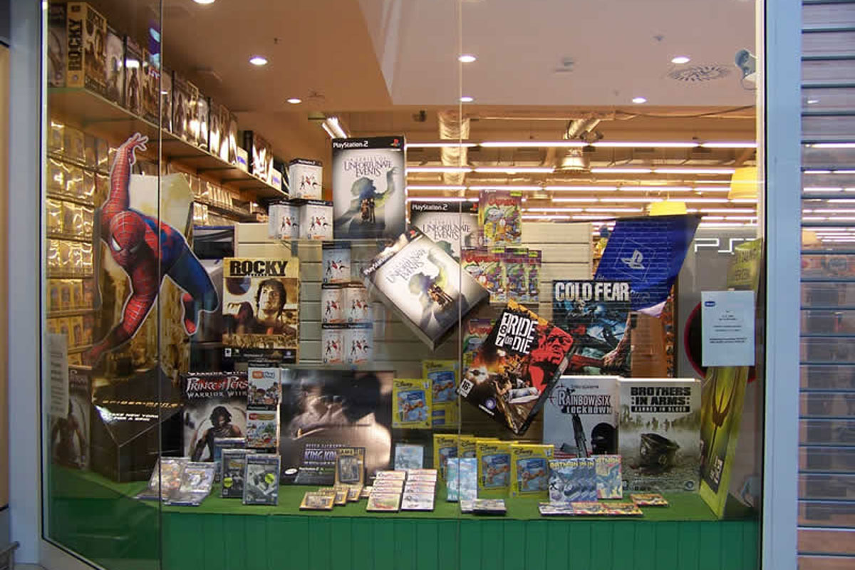 Prodejna CD, DVD videoher, aranžmá nosičů, krabic a maket ve výloze Výloha prodejny s videohrami, naaranžované makety, krabice a nosiče CD, DVD a dalších nosičů