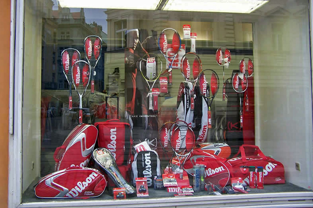 Výloha sportovní prodejny, aranžmá tenisových raket a výbavy pro tenis Prodejna sportovních potřeb část pro tenis, naaranžovaná výloha s nabídkou vybavení pro tenisty