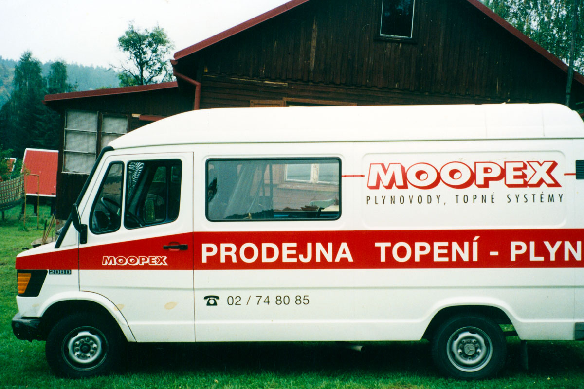 Dodávka Mercedes firmy Moopex, polepeno logem firmy a pruhy s nápisy Bílé auto Mercedes polepené logem Moopex a červenými pruhy s bílým textem