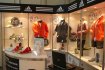 Vitríny a stolek na výstavní expozici s produkty Adidas, límce stánku vylepené logy Adidas